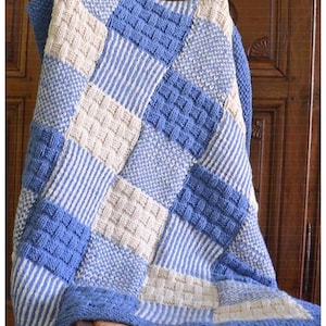 Könnte beinhalten: Eine handgefertigte Decke im Patchwork-Stil in Blau- und Cremetönen. Die Decke weist verschiedene strukturierte Quadrate und Streifen auf, die ein gemütliches und optisch ansprechendes Design ergeben. Die Kanten sind mit einem blauen Rand versehen.