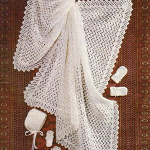 May include: A white, open-weave baby blanket with a scalloped edge, paired with a matching bonnet, booties, and mittens. The items are arranged on a patterned red and brown rug, creating a soft and delicate aesthetic.