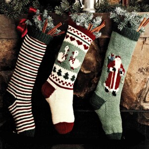 May include: Three festive Christmas stockings, each with a different pattern. One is striped, another has geese and trees, and the third shows Santa Claus. Cinnamon sticks and greenery are placed at the top of each stocking.