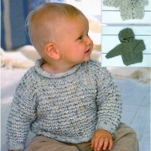 May include: A baby wearing a gray knit sweater with a round collar and long sleeves. The sweater has a textured pattern with flecks of gold and brown. Two additional knit baby sweaters are shown in the upper right corner, one with a hood.