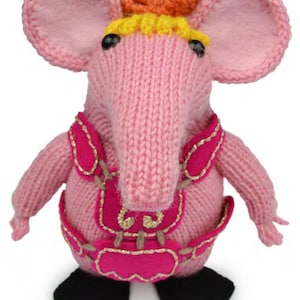 Puede incluir: Un juguete de elefante rosa tejido a mano con orejas grandes, una trompa larga y ojos negros. El elefante lleva un atuendo rosa con adornos dorados y pies negros. Un pequeño lazo naranja está en la parte superior de su cabeza.