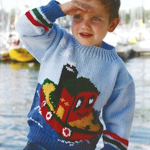 May include: A light blue knitted sweater with a colorful cartoon boat design on the front. The sweater has blue cuffs with red, green, and white stripes. The child is wearing blue jeans.