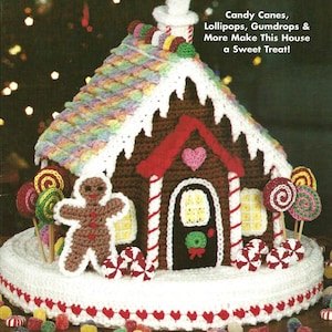 May include: A crocheted gingerbread house with a rainbow roof, white trim, and red accents. The house features a gingerbread man, lollipops, and candy canes. Text reads "Candy Canes, Lollipops, Gumdrops & More Make This House a Sweet Treat!"