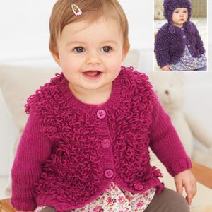 May include: A magenta baby cardigan with a textured, looped design around the collar and front. The cardigan has three matching buttons and long sleeves. A matching hat is shown in the inset. The baby is wearing a floral print top.