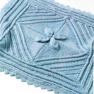 May include: A light blue knitted baby blanket with a four-petal flower design in the center. The blanket features a scalloped edge and various textured patterns. The text "Little boy blue" is visible in the upper left corner.
