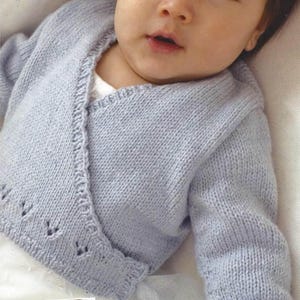 May include: A light blue knitted baby cardigan with a wrap-style design. The cardigan features a delicate scalloped edge and small decorative cutouts near the hem. The soft, pastel color and cozy knit suggest a focus on comfort and warmth for infants.