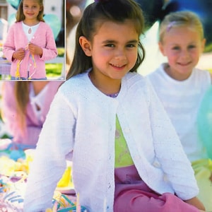 Puede incluir: Una niña pequeña con una rebeca blanca de punto con cierre de botones. La rebeca tiene un patrón diagonal texturizado en las mangas. También lleva una camisa verde claro y pantalones rosas. Una imagen más pequeña muestra una rebeca rosa.