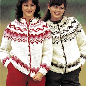 May include: Two women wearing white knit cardigans with geometric patterns in red, pink, and brown. The cardigans have button closures and are paired with red and dark trousers. The background is a blurred outdoor scene.