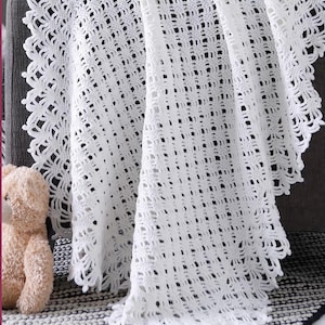 May include: A white, open-weave crochet blanket with a decorative scalloped edge is draped over a grey sofa. The blanket's texture is visible, and a small teddy bear sits nearby. The blanket is approximately 152 cm wide.