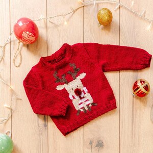 May include: A red knitted Christmas sweater featuring a reindeer design. The reindeer has a white face, brown antlers, and a red nose. Festive baubles and fairy lights are in the background.