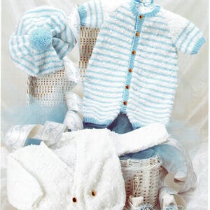May include: A collection of baby clothing, including a striped blue and white romper, a matching hat with a pom-pom, a white cardigan, and baby shoes. The items are displayed on a white surface with decorative ribbons and a wicker basket.