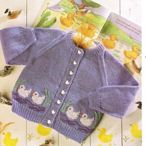 May include: A lilac knitted cardigan with a duck design. The sweater has white buttons and an embroidered pattern of ducks. The image also shows a children's book with duck illustrations. The text on the book reads "Four little ducks went swim Over the hills and far away."