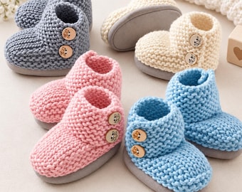 May include: Four pairs of knitted baby booties in blue, cream, pink, and light blue. Each pair features a thick garter stitch texture, a solid gray sole, and two wooden buttons on the side. The buttons are engraved with small bear or rabbit designs.