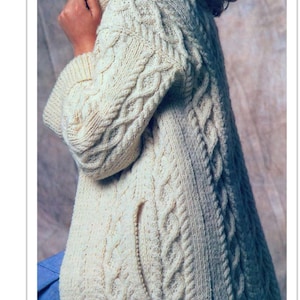 May include: Cream cable-knit sweater coat with a high collar and long sleeves. The coat features intricate cable patterns and a split hem. The garment is made of a thick, textured yarn, and has a pocket on the front.