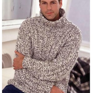 May include: A textured, gray and white knit turtleneck sweater. The sweater has a thick, cable-knit pattern and a high collar. The person in the image is wearing blue jeans. The sweater appears to be made of a warm, wool-like material.