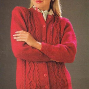 May include: A red cable-knit cardigan with a button-up front. The sweater has a round neckline and long sleeves. The woman in the image is wearing a floral print scarf and earrings.