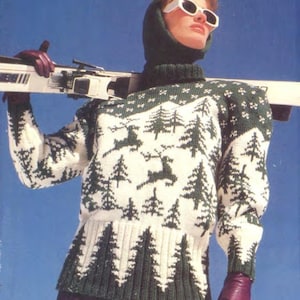May include: A white and green knit sweater with a forest and deer pattern. The sweater has a high neck and is worn with a matching hood and sunglasses. The person is holding skis and wearing purple gloves.