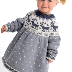 Pode incluir: Vestido cinzento de malha com um padrão de renas na pala e bolinhas brancas na saia. O vestido tem mangas compridas e decote redondo. A barra é branca e azul marinho. Uma criança pequena está a usar o vestido.