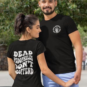 May include: Two people wearing black t-shirts. The back of the first shirt says "DEAD PEDOPHILES DON'T OFFEND" in white text. The front of the second shirt has a graphic with the text "DEAD PEDOPHILES DON'T REOFFEND".