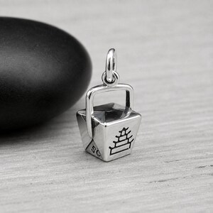 Puede incluir: Un dije de plata con forma de recipiente de comida para llevar con un asa y una argolla en la parte superior. El lateral del recipiente presenta un gr&aacute;fico grabado en negro de una pagoda de varios niveles y los caracteres 5G en la esquina.