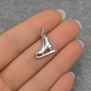 Peut inclure: Un petit pendentif argent&eacute; brillant en forme de patin &agrave; glace. Ce bijou pr&eacute;sente une silhouette de botte d&eacute;taill&eacute;e avec des lacets visibles et une lame &agrave; la base, surmont&eacute; d'un petit anneau de jonction circulaire pour le suspendre.