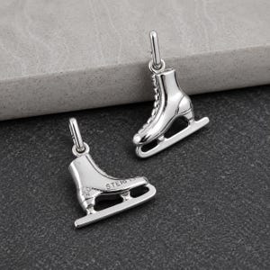 Peut inclure: Deux breloques en forme de patins &agrave; glace argent&eacute;s, dot&eacute;es d'une finition m&eacute;tallique polie et d'un petit anneau de jonction sur le dessus. Une breloque est orient&eacute;e verticalement, tandis que l'autre est horizontale, avec le texte STERLING grav&eacute;.