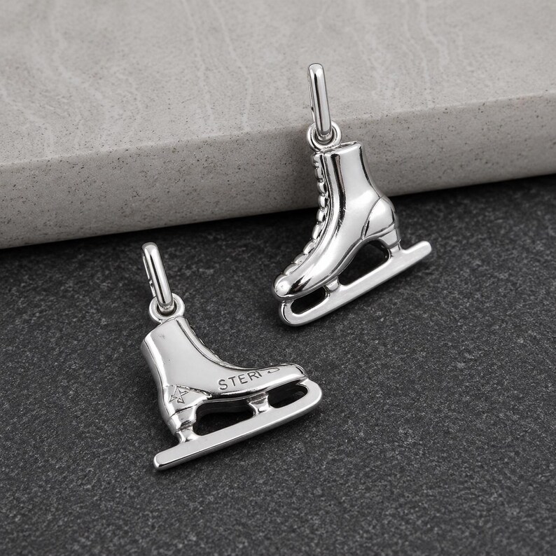Peut inclure: Deux breloques en forme de patins &agrave; glace argent&eacute;s, dot&eacute;es d'une finition m&eacute;tallique polie et d'un petit anneau de jonction sur le dessus. Une breloque est orient&eacute;e verticalement, tandis que l'autre est horizontale, avec le texte STERLING grav&eacute;.