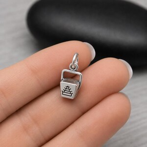 Puede incluir: Un peque&ntilde;o dije de plata con forma de recipiente de comida para llevar con un asa en la parte superior. El frente del recipiente presenta un gr&aacute;fico grabado en negro de una pagoda de varios niveles. El dije incluye una peque&ntilde;a argolla de plata.