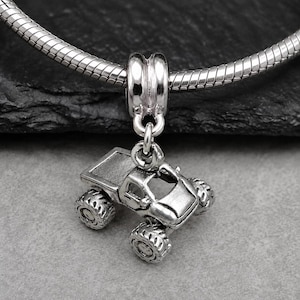 May include: A silver-toned metal charm shaped like a monster truck with large, textured tires and an open-cab design. The charm is suspended from a polished silver-toned metal bail, which is threaded onto a flexible, snake-style silver chain necklace.