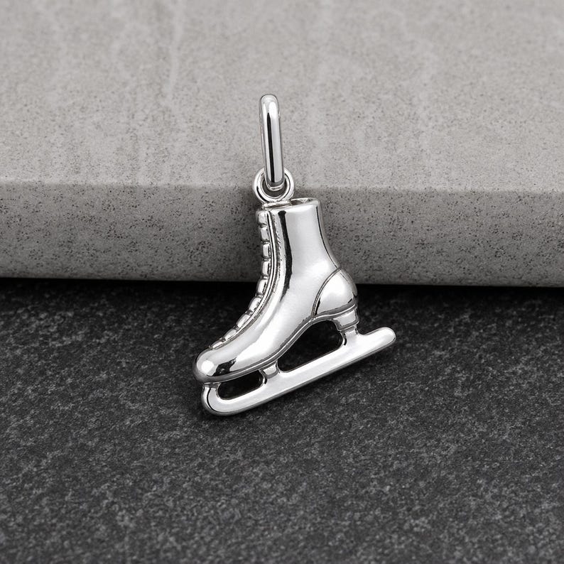 Peut inclure: Un charm en m&eacute;tal argent&eacute; poli en forme de patin &agrave; glace. Le bijou pr&eacute;sente une botte d&eacute;taill&eacute;e avec des lacets visibles et une lame lisse fix&eacute;e &agrave; la base. Un petit anneau circulaire est fix&eacute; sur le dessus pour permettre de le suspendre.