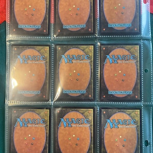 May include: Nine Magic: The Gathering cards in a clear plastic page protector. The cards are all black and red with gold accents and feature the Magic: The Gathering logo.