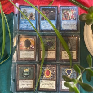 May include: A collection of Magic: The Gathering cards in a binder. The cards are all black bordered and feature various illustrations of artifacts and spells. The cards are organized by color and type.