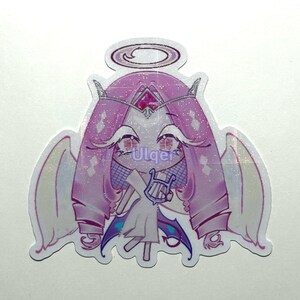 K&ouml;nnte beinhalten: Ein Aufkleber mit einem Cartoon-Engel mit Heiligenschein, Fl&uuml;geln und einer Harfe. Der Engel hat rosa Haare, Augen und eine Krone. Der Aufkleber hat ein glitzerndes Finish und den Text "Ulqer".