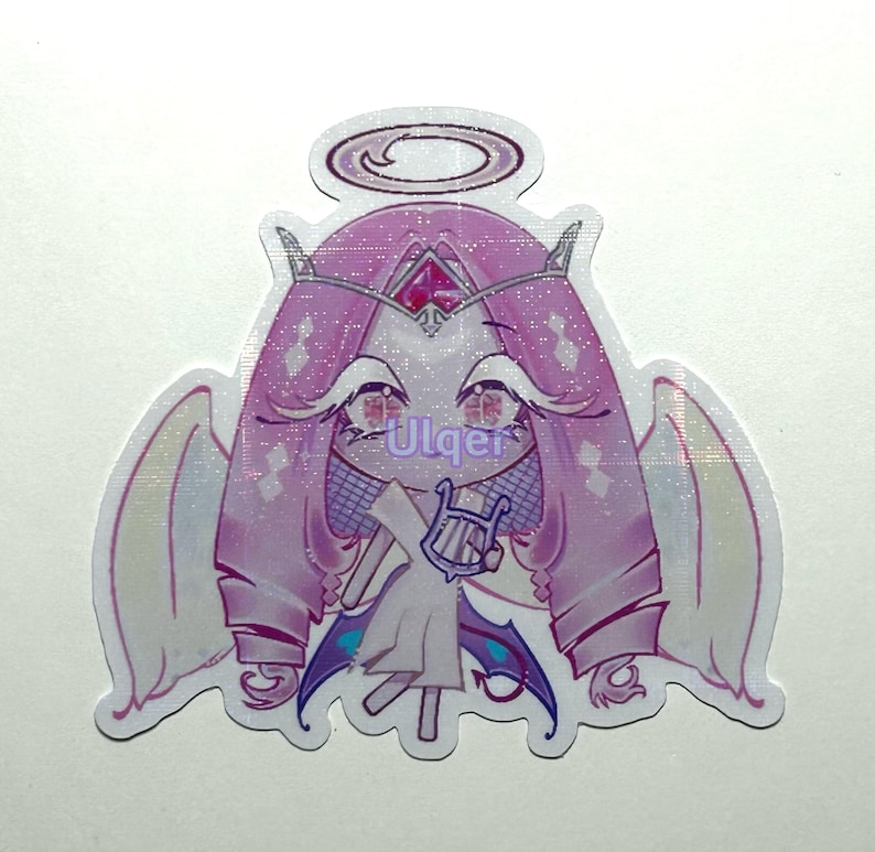 K&ouml;nnte beinhalten: Ein Aufkleber mit einem Cartoon-Engel mit Heiligenschein, Fl&uuml;geln und einer Harfe. Der Engel hat rosa Haare, Augen und eine Krone. Der Aufkleber hat ein glitzerndes Finish und den Text "Ulqer".