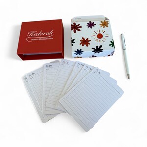 May include: A red box with the text Kedarah Boston, Massachusetts, a white box with a colorful floral pattern, a silver pen, and several white to-do list cards with lines and the text To-Do and Date printed at the top of each individual card.