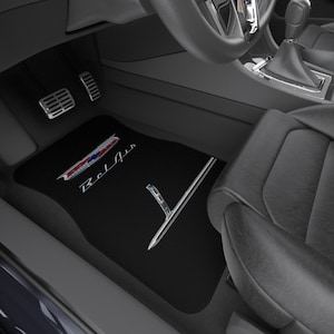 May include: Black car floor mat with the word "Bel Air" in white script. The mat has a chrome accent and a red, white, and blue emblem. The mat is in a car interior with pedals and a seat visible.