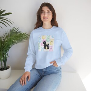 May include: A light blue sweatshirt with a graphic print of a black poodle surrounded by pastel-colored bunny-shaped marshmallows.