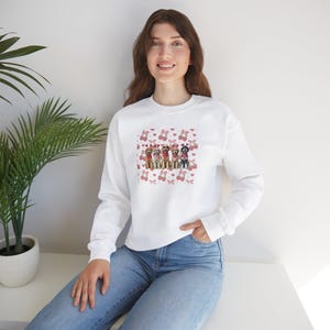 May include: White sweatshirt with a pink and white pattern of hearts and bows. The center of the sweatshirt features a graphic of six dogs wearing red bandanas.