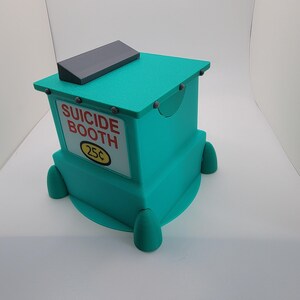 Op de afbeelding: Een turquoise kraam met een grijs dak en afgeronde voetjes. Op het bord staat "SUICIDE BOOTH" met "25&cent;" eronder. De kraam heeft een boxy ontwerp met een kleine, gebogen uitsparing aan de zijkant.