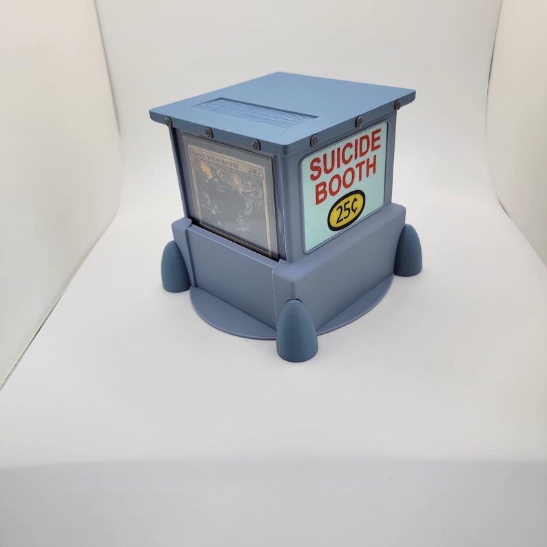 Op de afbeelding: Een lichtblauwe, doosvormige display met een kaart zichtbaar aan de binnenkant. De behuizing heeft de woorden "SUICIDE BOOTH" en "25&cent;" op de zijkant gedrukt. De behuizing heeft een platte bovenkant en vier afgeronde voetjes.