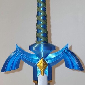 May include: A blue and silver Master Sword replica with a green rope handle. The sword has a diamond-shaped gem in the center of the hilt.