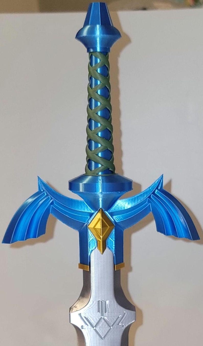 May include: A blue and silver Master Sword replica with a green rope handle. The sword has a diamond-shaped gem in the center of the hilt.