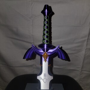 May include: A purple and silver 3D printed sword with a green rope handle. The sword has a diamond-shaped design on the blade and a winged hilt.