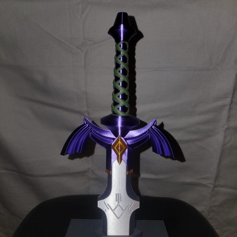 May include: A purple and silver 3D printed sword with a green rope handle. The sword has a diamond-shaped design on the blade and a winged hilt.