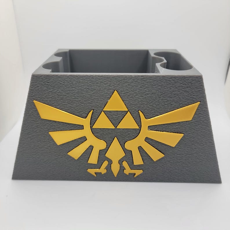 May include: A gray 3D printed game cartridge holder with a gold Triforce logo. The holder has slots for multiple cartridges.