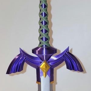 May include: A purple and gold 3D printed sword with a green braided handle. The sword has a diamond-shaped guard and two wings on either side of the blade.