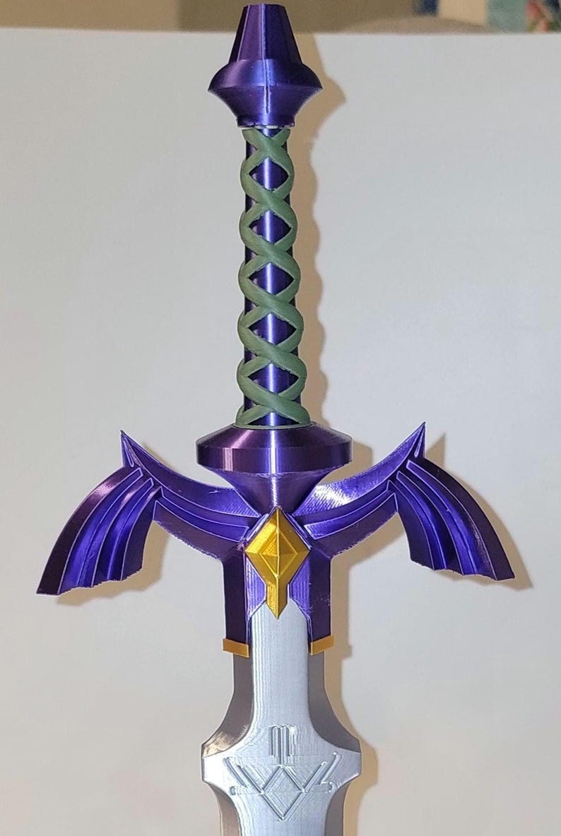 May include: A purple and gold 3D printed sword with a green braided handle. The sword has a diamond-shaped guard and two wings on either side of the blade.