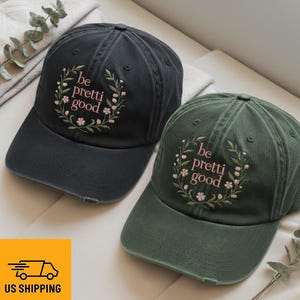 Puede incluir: Se muestran dos gorras de béisbol, una negra y otra verde. Cada gorra presenta la frase bordada "be pretty good" dentro de una corona floral. Las gorras tienen un aspecto desgastado, con una apariencia ligeramente usada.