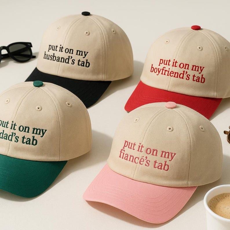 Puede incluir: Cuatro gorras de b&eacute;isbol beige con viseras de diferentes colores. Cada gorra tiene la frase "put it on my" seguida de "husband's tab", "boyfriend's tab", "dad's tab" y "fianc&eacute;'s tab" bordada en un color a juego.