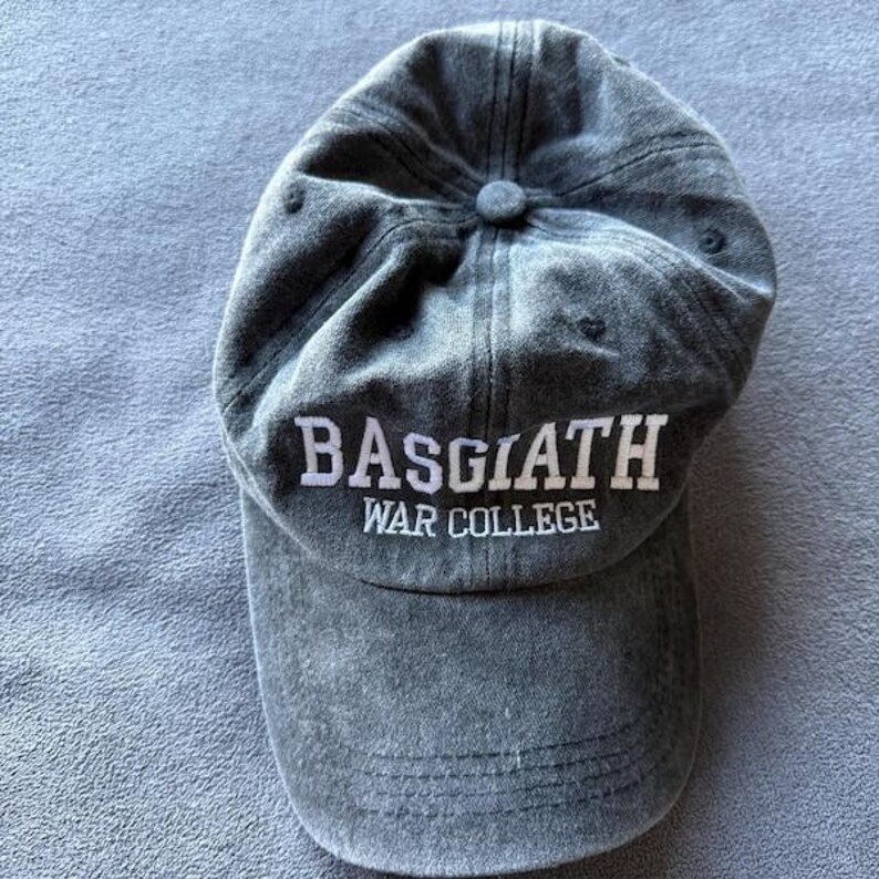 May include: A gray baseball cap with the text "BASGIATH WAR COLLEGE" in white lettering. The cap has a curved brim and a button on top. The fabric appears to be a soft, worn material.